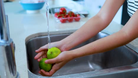 hands thoroughly rinse green limes under running water in a modern kitchen sink, with natural daylight and a shallow depth of field highlighting the cleaning process