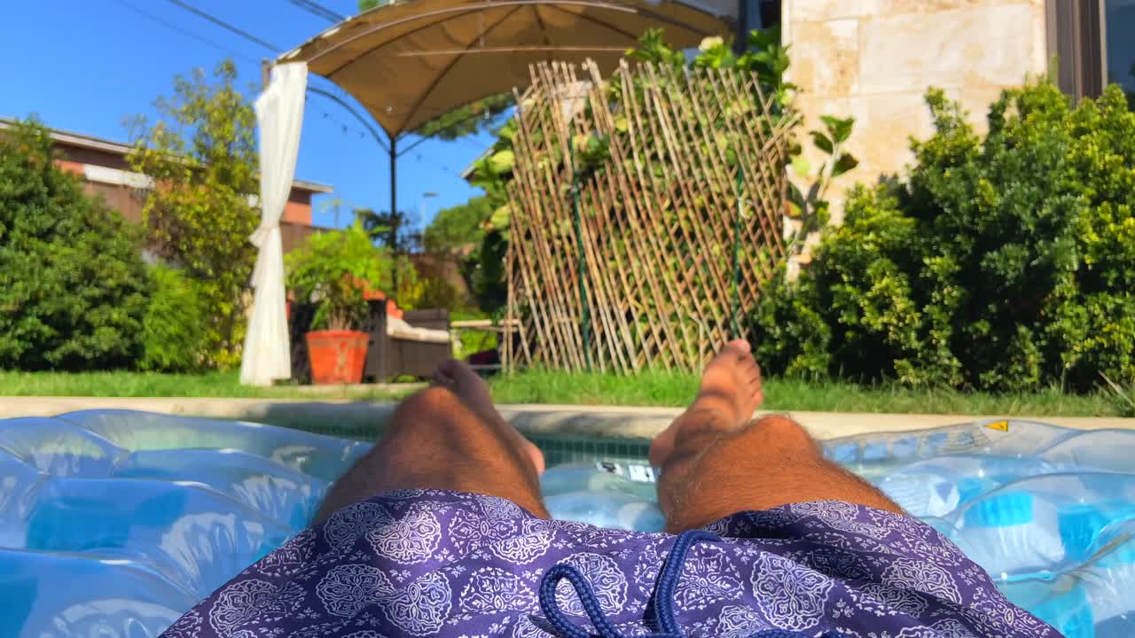 4K slow-motion footage of a guy relaxing on a mat sunbathing in the pool of a large and modern villa of Pozuelo de Alarcón, Spain. Concept of luxury neighborhood in Spain.