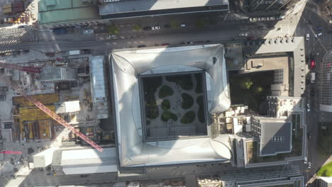 Birds-Eye-View-looking-down-on-Office-Buildings-in-City-with-construction-site-crane-and-garden,-Aerial-Drone-perspective