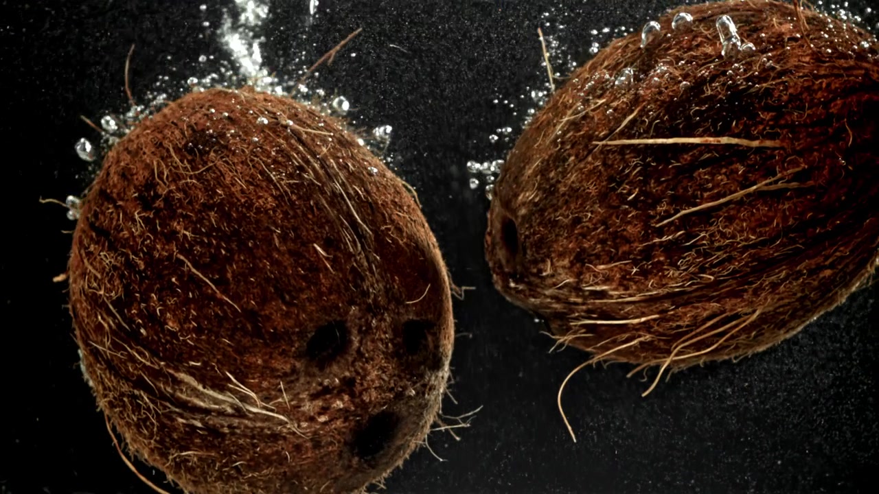 Two Coconuts Sinking into Water with Bubbles on Black Background
