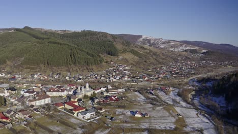 Vista-De-Drones-De-Padure---Ciudad-En-El-Valle-Debajo-De-Una-Cordillera-Bordeada-De-Pinos-Y-Nieve