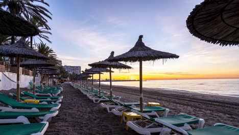 time lapse sunrise on marbella beach with sun beds and sun umbrellas, holiday destination 4k