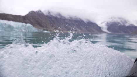 bow waves of motorboat sailing under glacier in cold sea water, slow motion