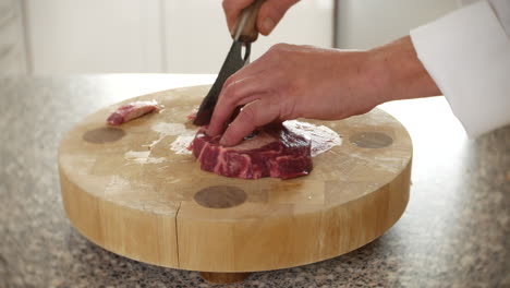 a chef is chopping and slicing a beef rib eye steak in a kitchen on a chopping board with a knife