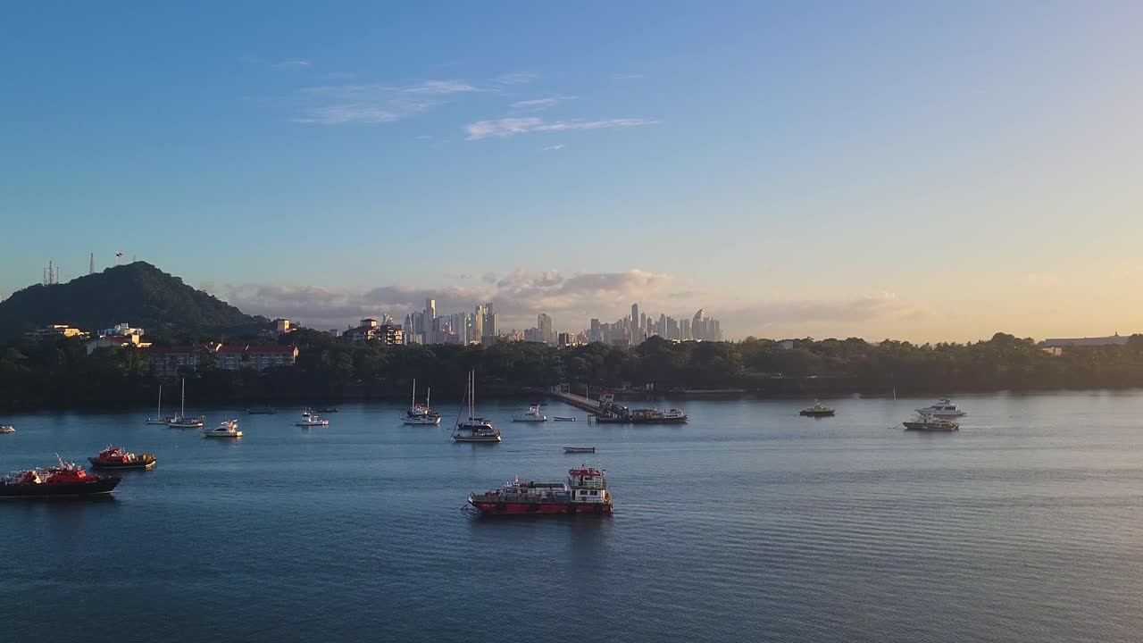 Numerous yachts and pleasure craft are moored in the calm waters of the Port of Balboa anchorage at sunrise, with Ancón Hill and the Panama City skyline creating a stunning backdrop.