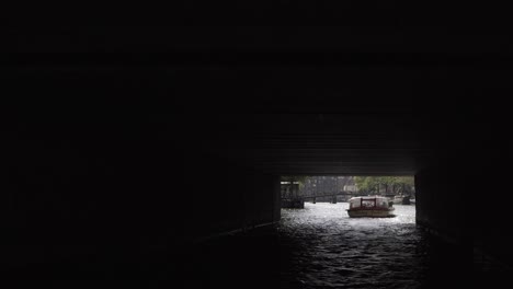 Typical-boat-cruise-on-the-famous-canals-of-amsterdam,-passing-bridges