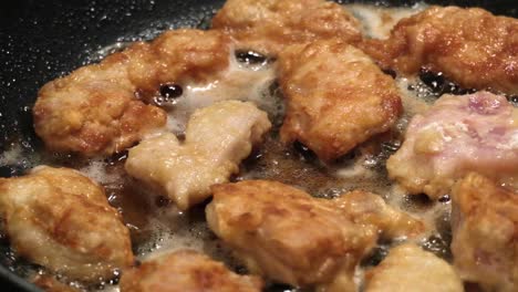 close up on chicken nuggets cooking in hot oil in a frying pan, slow motion