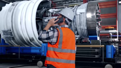 back view of asian male engineer with safety helmet talking on smartphone while standing with airplane engine maintenance conducted, analytics checking the turbine