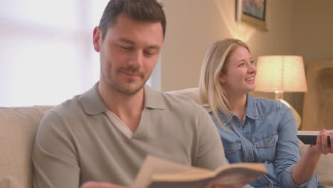 evening shot of couple relaxing on sofa at home with man reading book and woman watching tv - shot in slow motion