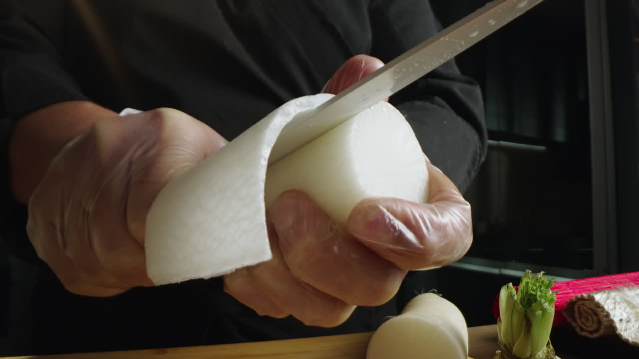 Close-up of a chef's gloved hands peeling a radish