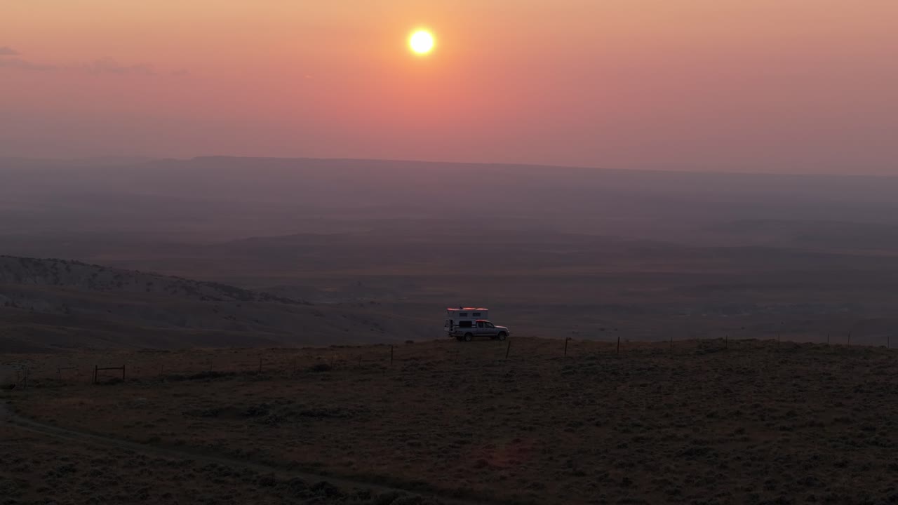 넓은 사막 풍경 위에 부드러운 빛으로 해가 지는 언덕에 주차 된 캠퍼