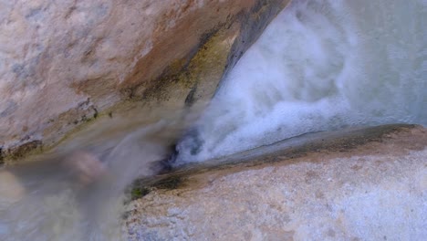 Small-stream-of-fast-flowing-waterfall-whitewater-cascade-over-naturally-formed-smooth-carved-by-water-deep-within-canyon