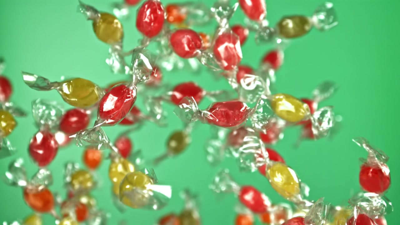 Caramelle colorate incartate che cadono al rallentatore su sfondo verde