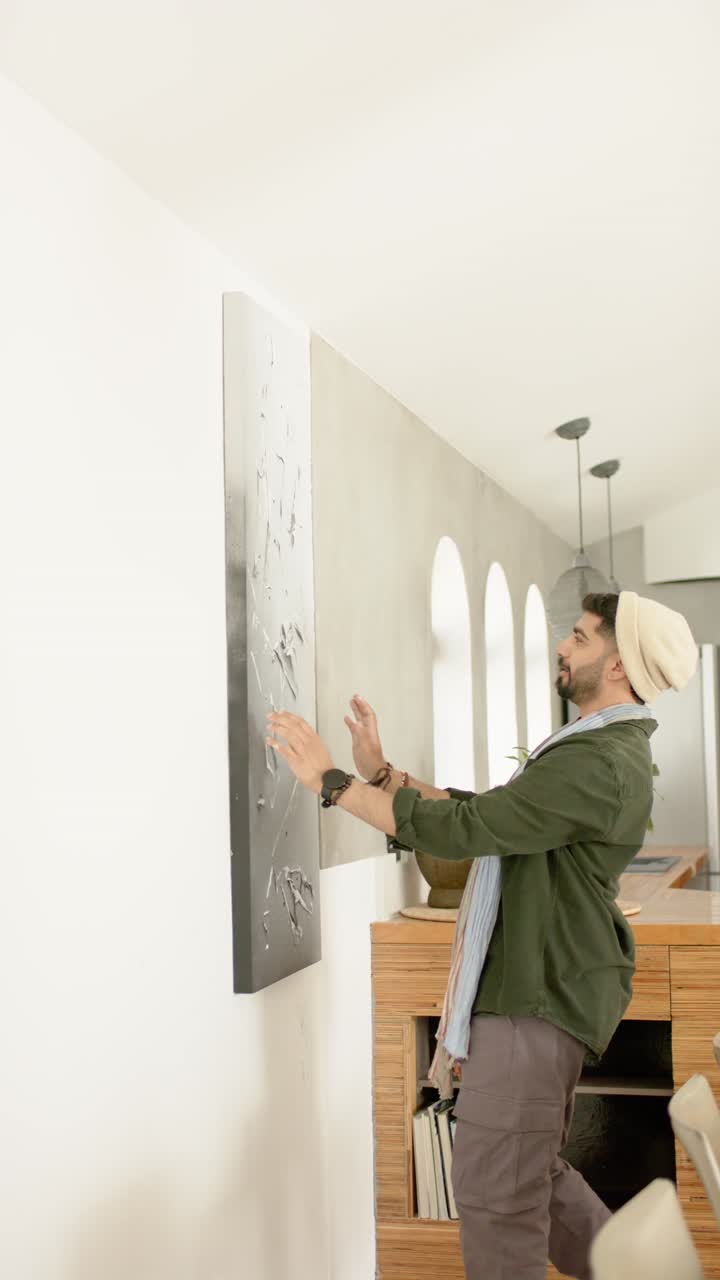Video verticale: uomo che entra in casa con un’area di lavoro artistica e si posiziona sul muro per appendere l’opera d’arte, spazio per la copia
