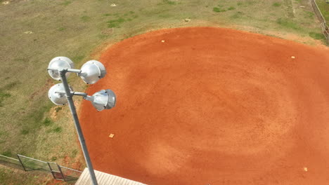 Toma-Aérea-De-Arriba-Hacia-Abajo-De-Las-Luces-Del-Estadio-Y-Campo-De-Béisbol-Vacío-Durante-El-Día-Soleado-En-América