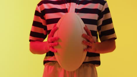 caucasian female rugby player with rugby ball over neon yellow lighting