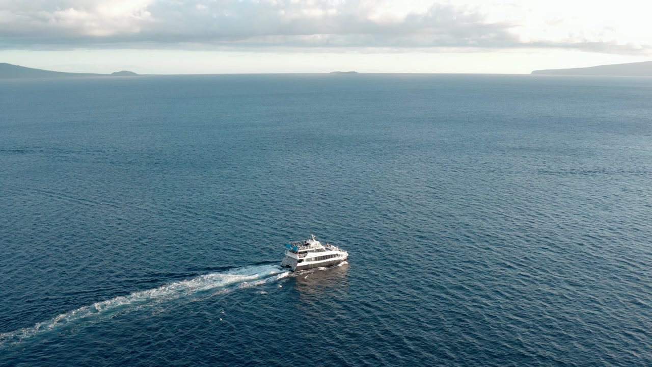 Static aerial shot white boat sailing across blue ocean with distant island and calm water