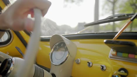 close up of steering wheel and hand driving classic yellow fiat car in europe traveling during the day