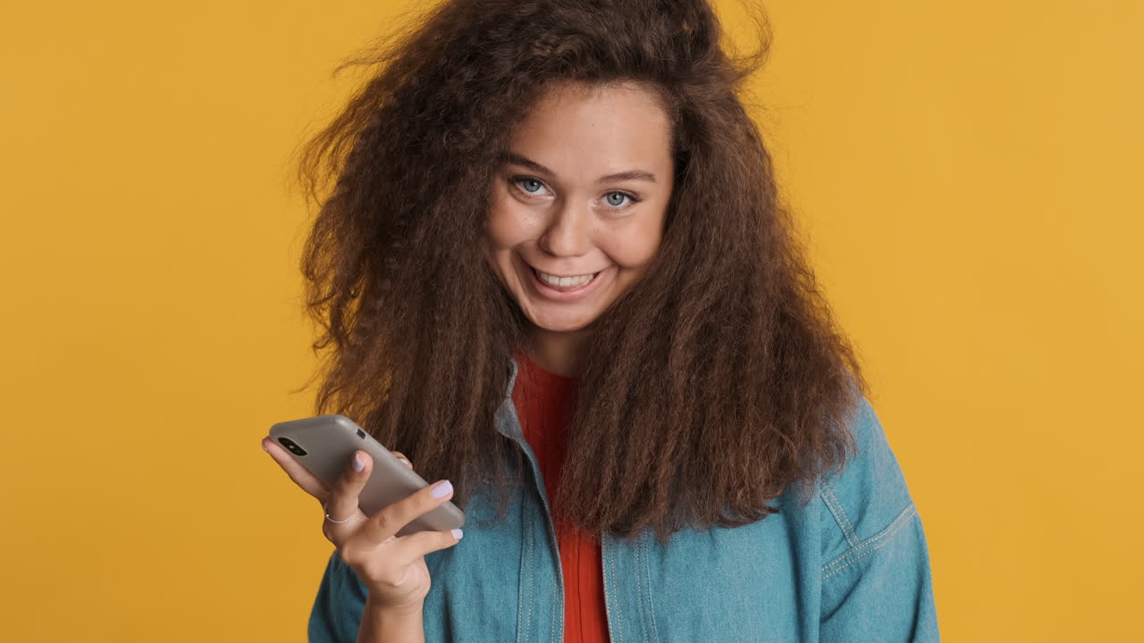 Caucasian curly haired woman using smartphone and smiling to camara.