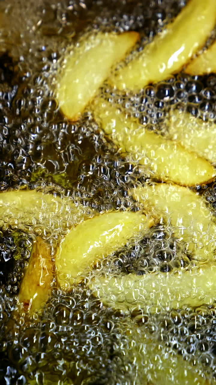 Crispy potato in boiling oil. Bubbles of hot oil during cooking french fries in deep fryer. Process of cooking golden fried potatoes. Macro shot. Vertical video