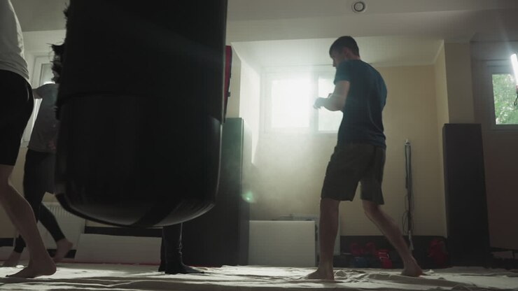 Sportsman kicks pad held by instructor in sports club. Young athlete trains fighting technique with team in gym slow motion. Martial arts workout
