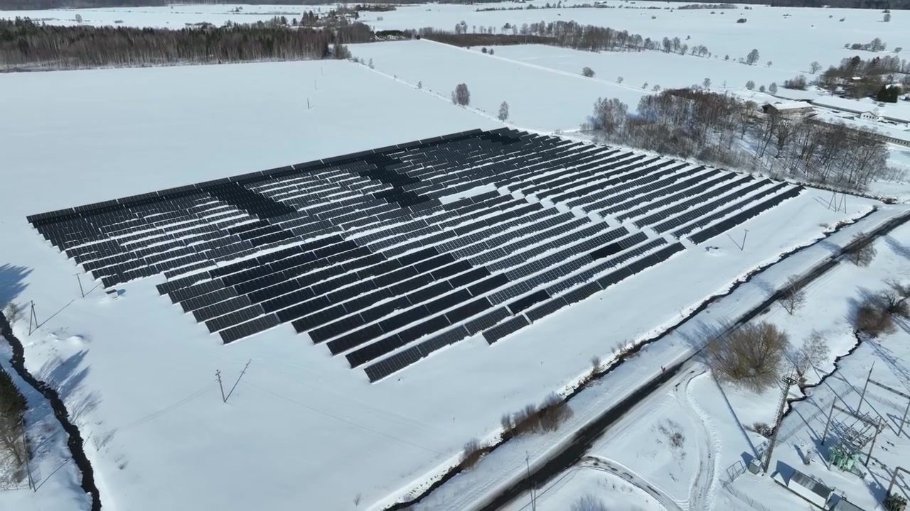 Dron letící pozpátku nad panely solární elektrárny v řadě na zasněžených polích. Haljala, Estonsko