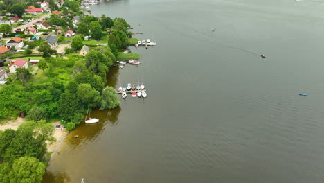 aerial view of a peaceful lakeside village with small boats docked along a shoreline surrounded by lush green trees and houses, showcasing serene nature and tranquility