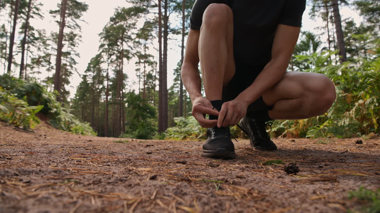 primer plano de un hombre atando los cordones de su zapato de entrenamiento antes de ejercitarse corriendo por la pista a través de un bosque filmado en tiempo real