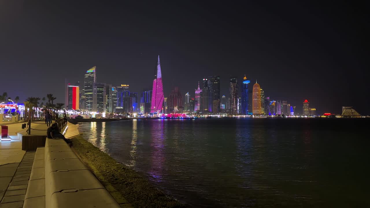 Doha-stranden om natten reflekterer den vakre Corniche-sjøbyens sentrum. Et moderne bylandskap for en trygg reise og naturskjønn spasertur i bybildet, med høye tårn, hoteller og handelsbygninger med moderne arkitektonisk design.