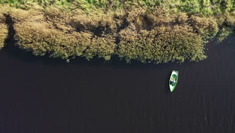 top up shot and moving on side with man on fishing boat who are fishing in the river near reeds