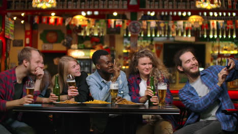 Friends-take-pictures-on-the-phone-at-the-bar-make-a-shared-photo-on-the-phone.-Party-with-friends-at-the-bar-with-beer.