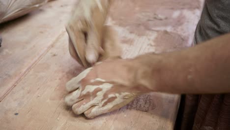 potter kneads clay with his hands on a wooden table