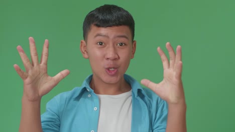 the shocked young asian boy grabbing his head while saying wow on green screen background in the studio