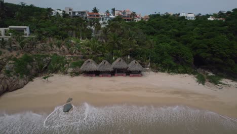 Luftaufnahme-Einiger-Strandhütten-In-Huatulco-Am-Ende-Des-Tages,-Während-Die-Wellen-Am-Ufer-Krachen