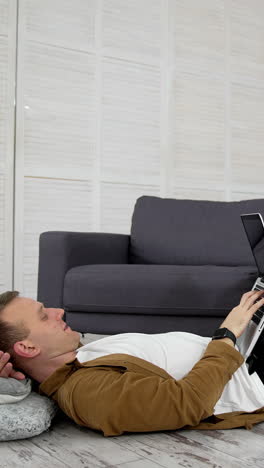 remote job. tired freelancer works on a laptop while lying on the floor in the kitchen. young man studying through the laptop at home. distance education. vertical video
