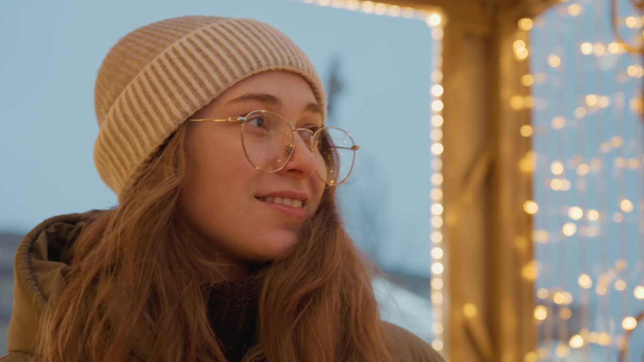 Donna caucasica che guarda luci scintillanti, con un sorriso gioioso, parka e berretto di lana, occhiali rotondi che catturano il bokeh dorato, sfondo urbano serale, atmosfera festiva e speranzosa, primi piani intimi.