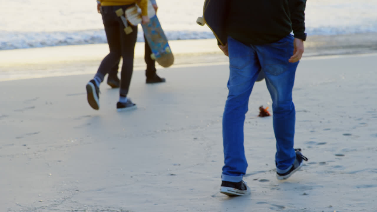 해가 지는 동안 해변에서 함께 산책하는 젊은 백인 친구들의 뒷면 4k