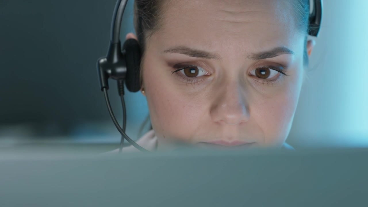 Hearing alert woman with headset leaning toward monitor at desk reading data and planning reply
