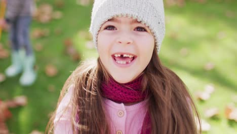 video of happy caucasian girl in woolly hat and scarf throwing autumn leaves in garden