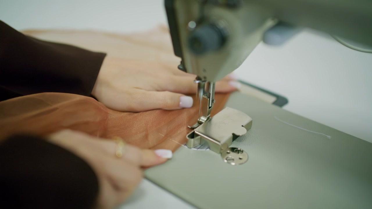 Primer plano de una persona guiando tela transparente marrón bajo la aguja de una máquina de coser industrial