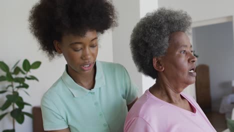 Happy-african-american-female-physiotherapist-helping-senior-female-patient-exercise-at-home