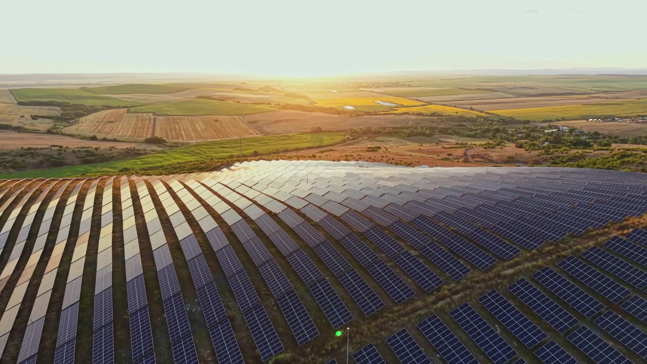 Solpaneler dækker et stort område, mens solen går ned over et landligt landskab fyldt med landbrugsjord