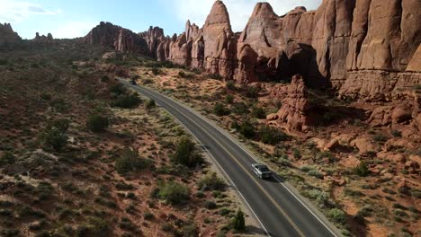 a cinematic drone recording capturing a convertible car as it travels through the stunning landscape of arches national park