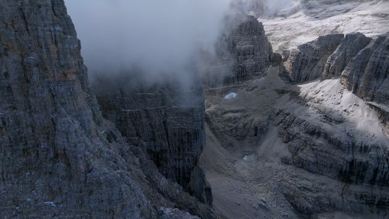 vuelo aéreo hacia adelante a lo largo de montañas rocosas con nubes flotantes en dolomitas italianas