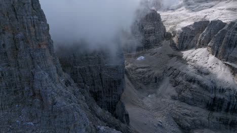 aerial forward flight along rocky mountains with hovering clouds in italian dolomites