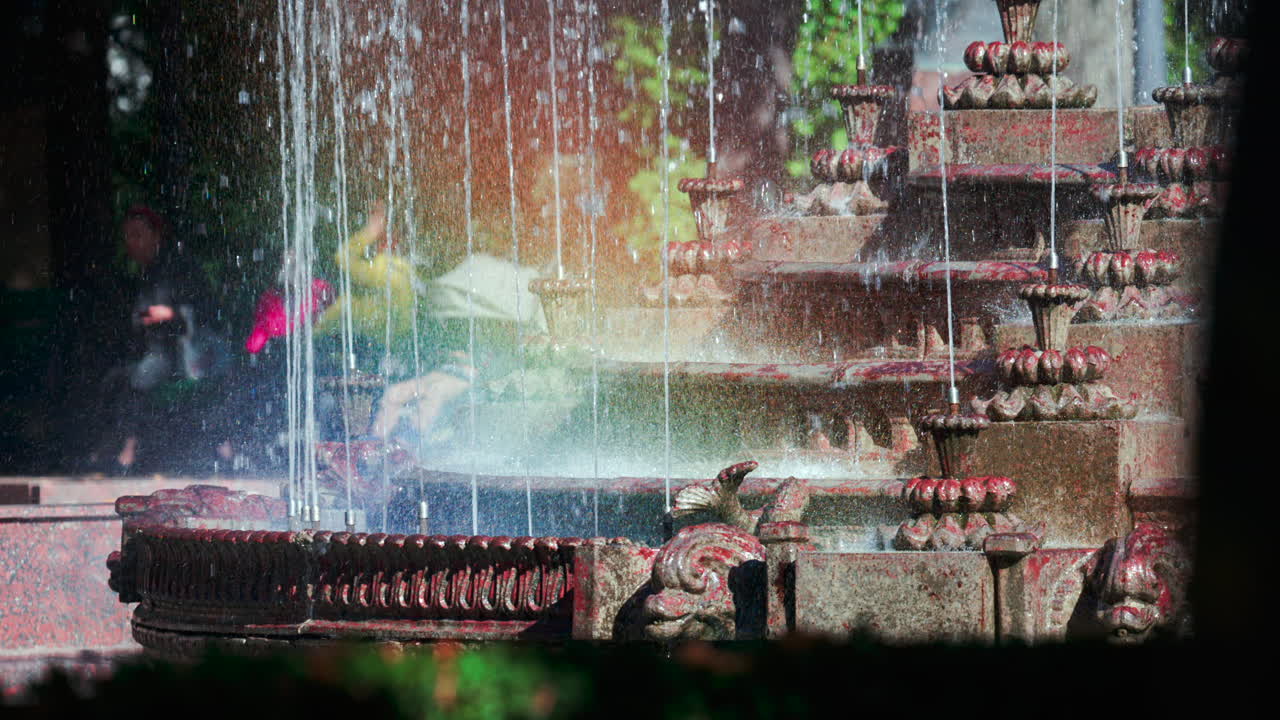 View of a decorative fountain with sparkling water droplets illuminated by sunlight in a park