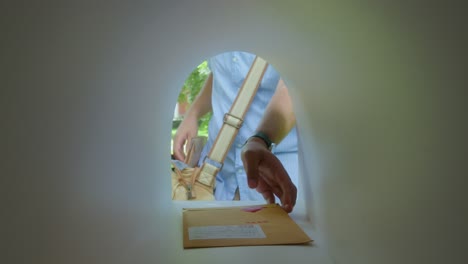 hands of postal worker placing envelopes into mailbox