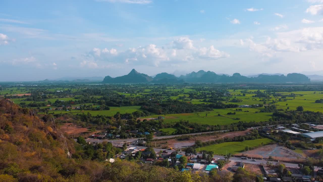 Une vue depuis un sommet en Thaïlande, surplombant des rizières verdoyantes et des montagnes imposantes au loin, entourées d'une forêt colorée.