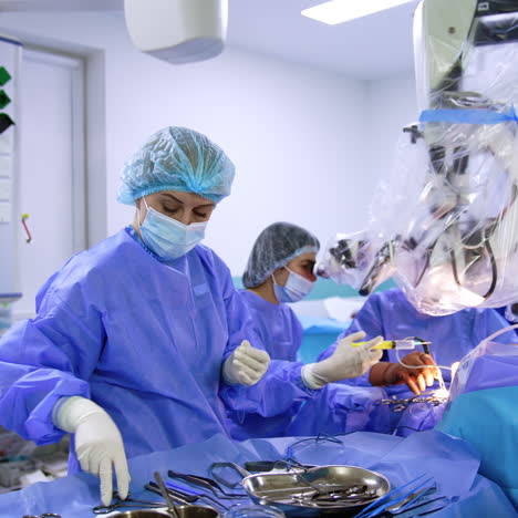 nurse assisting at neurosurgical operation prepares tools and materials for the doctor. surgeon operating the patient looks at microscope.