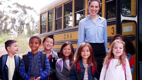 school teacher and  schoolchildren in front of school bus